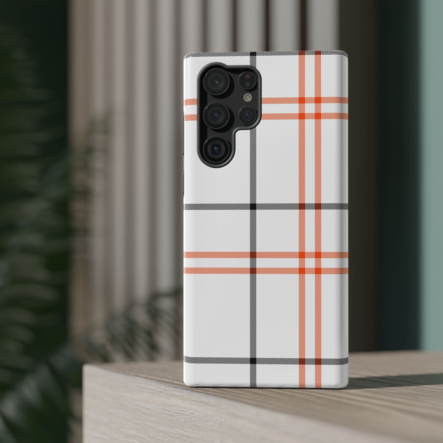 A phone case with a fall tartan plaid pattern in white and orange stripes, featuring a camera module in the center.