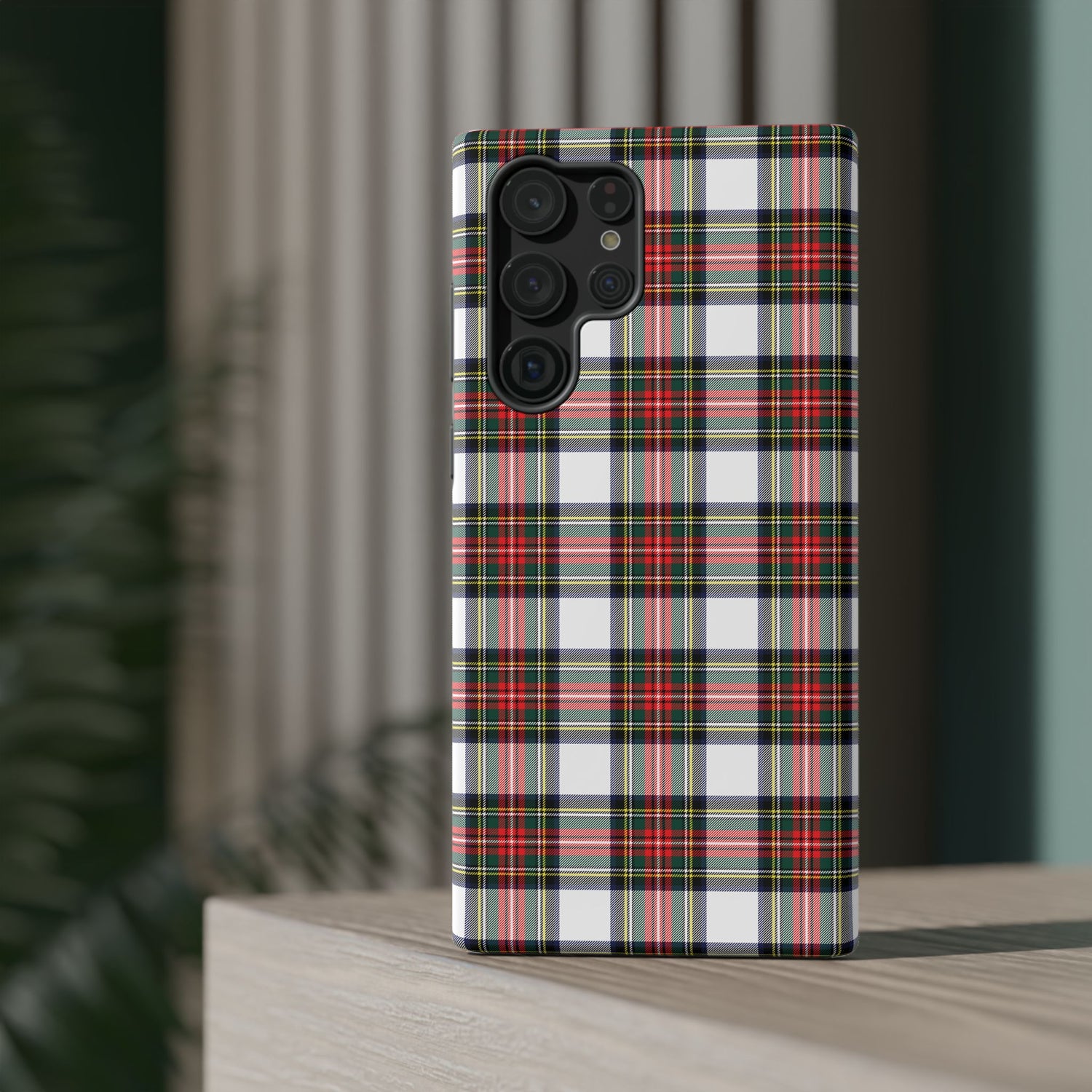 A phone case with a Christmas tartan plaid design, featuring a camera module on the back, placed on a wooden surface with a blurred background.