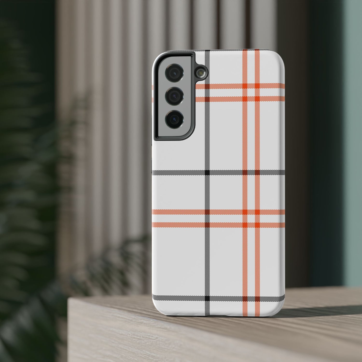 A phone case with a fall tartan plaid pattern in white and orange stripes, featuring a camera module in the center.