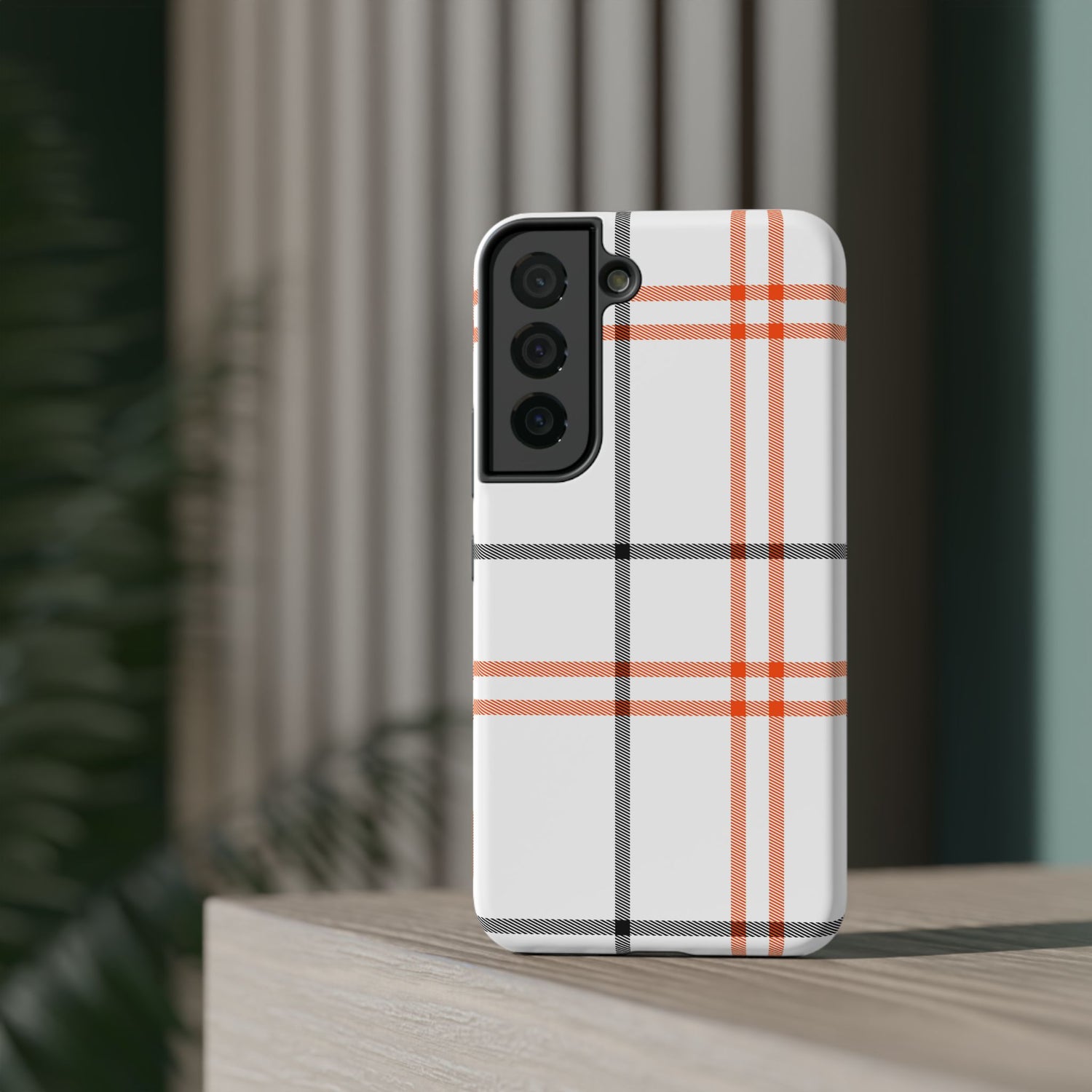 A phone case with a fall tartan plaid pattern in white and orange stripes, featuring a camera module in the center.