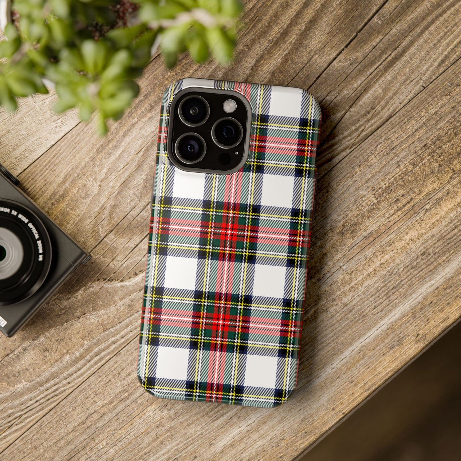 A phone case with a Christmas-themed tartan plaid design, placed on a wooden surface next to a camera, showcasing its impact-resistant features.
