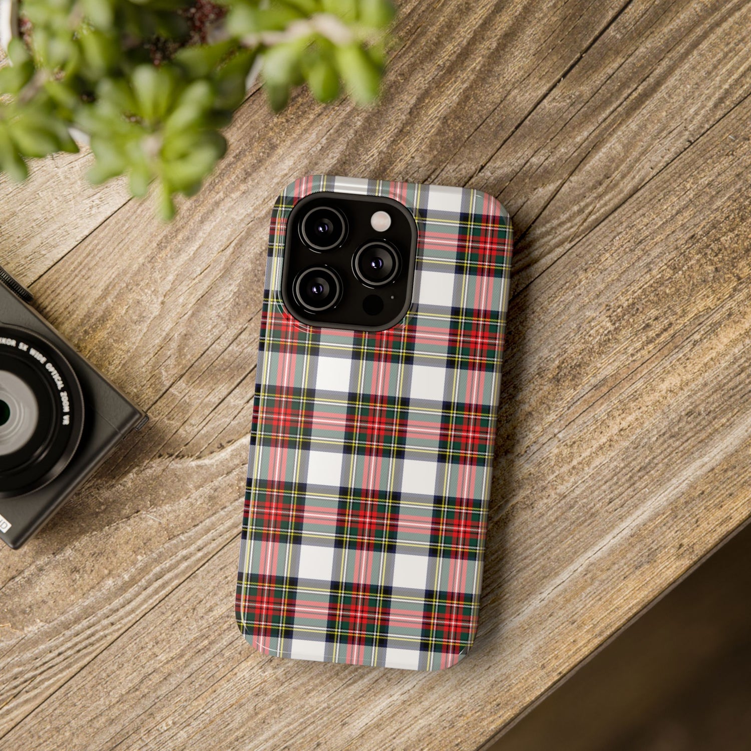 A phone case with a Christmas tartan plaid design, placed on a wooden surface next to a camera, showcasing its impact-resistant features.