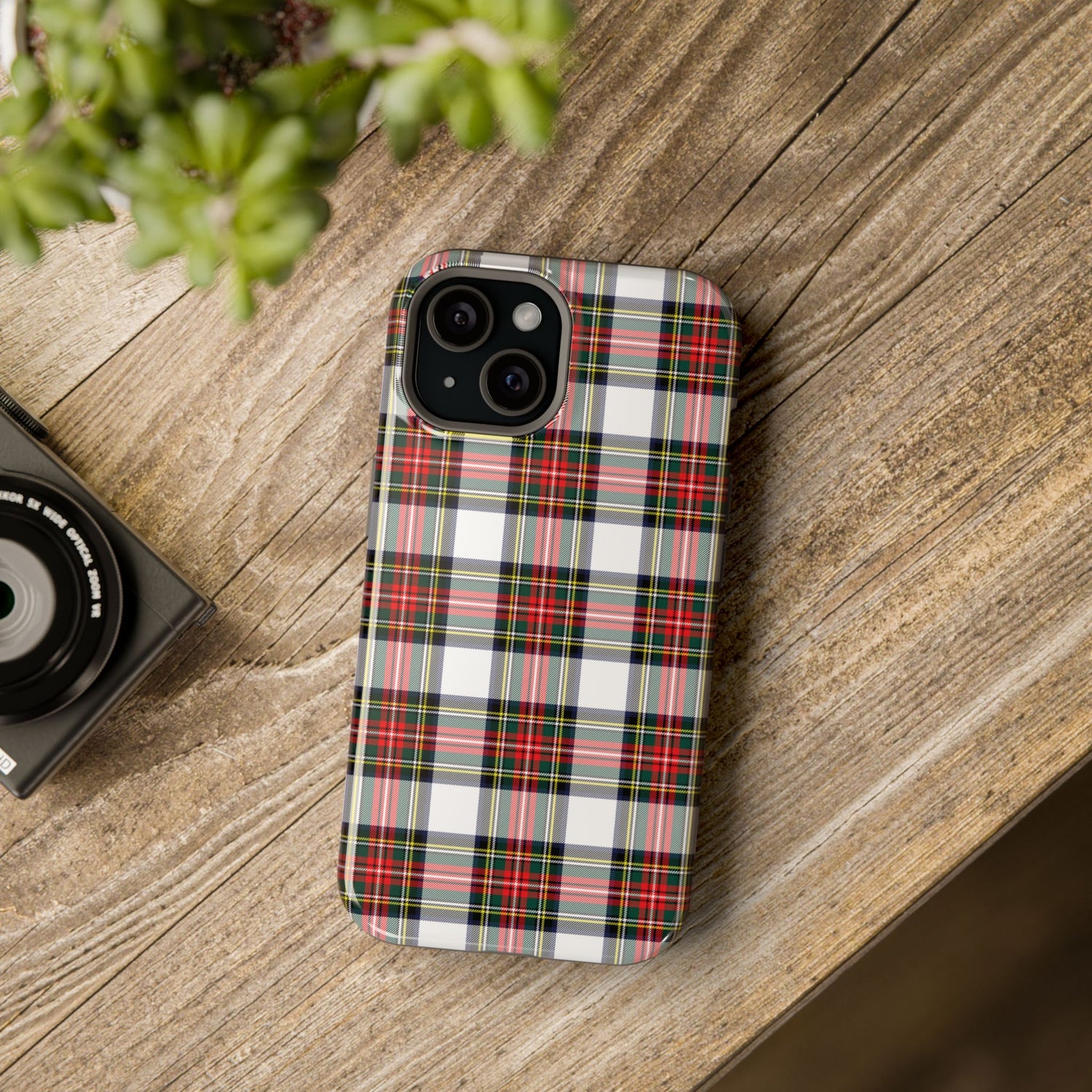 A phone case with a red and black tartan pattern design, placed on a wooden surface next to a camera.