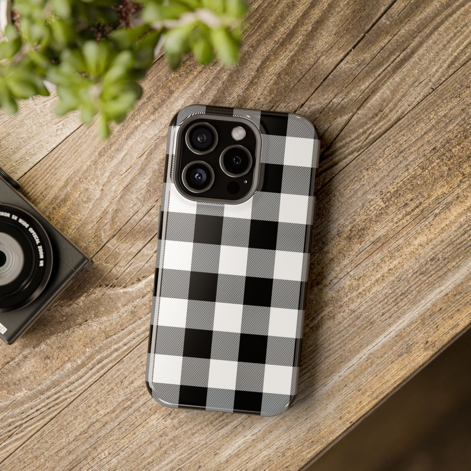 A black and white checkered phone case with a camera module on top, placed on a wooden surface next to a small camera.