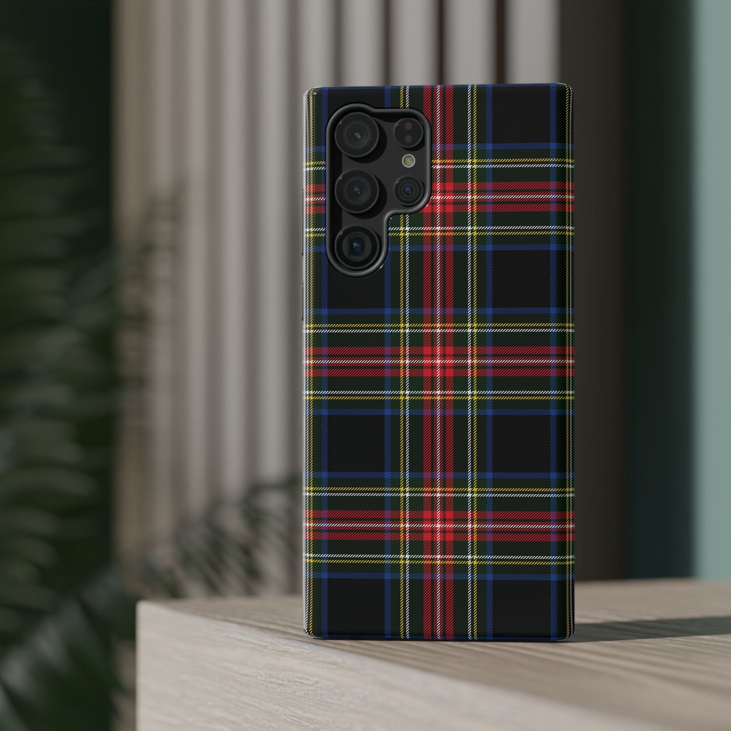A phone case with a Christmas-themed tartan plaid pattern in black, red, and green, placed on a wooden surface with a blurred background.
