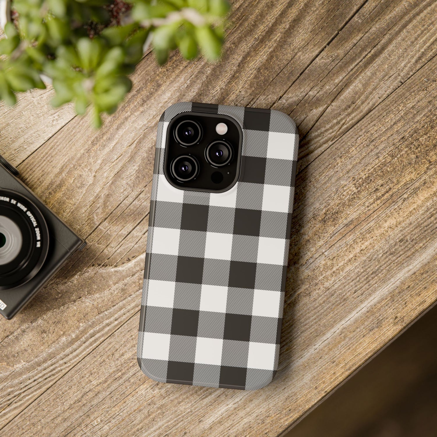 A black and white checkered phone case with a camera module on top, placed on a wooden surface next to a small camera.