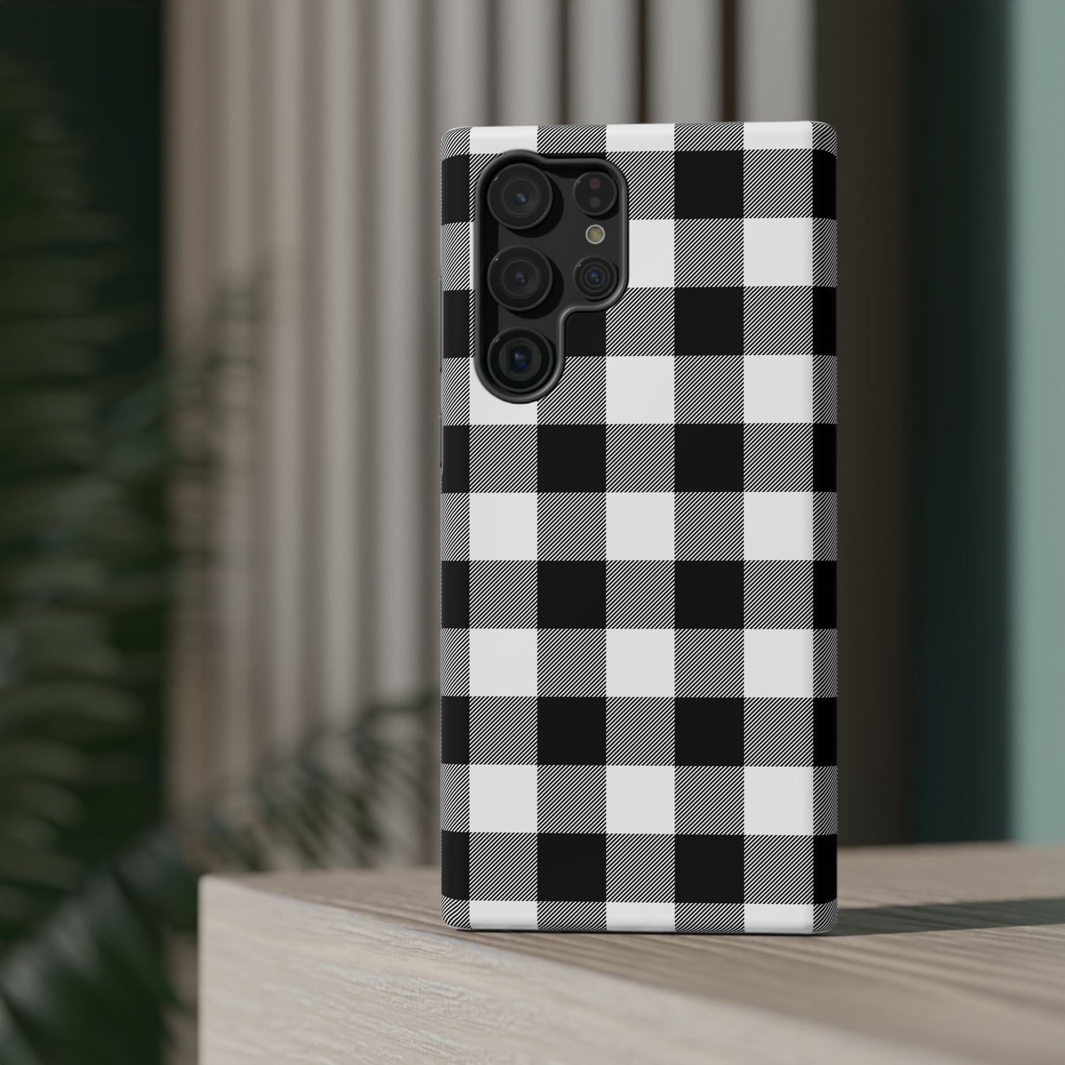 A black and white checkered phone case with a camera module on the back, placed on a wooden surface with a blurred background.