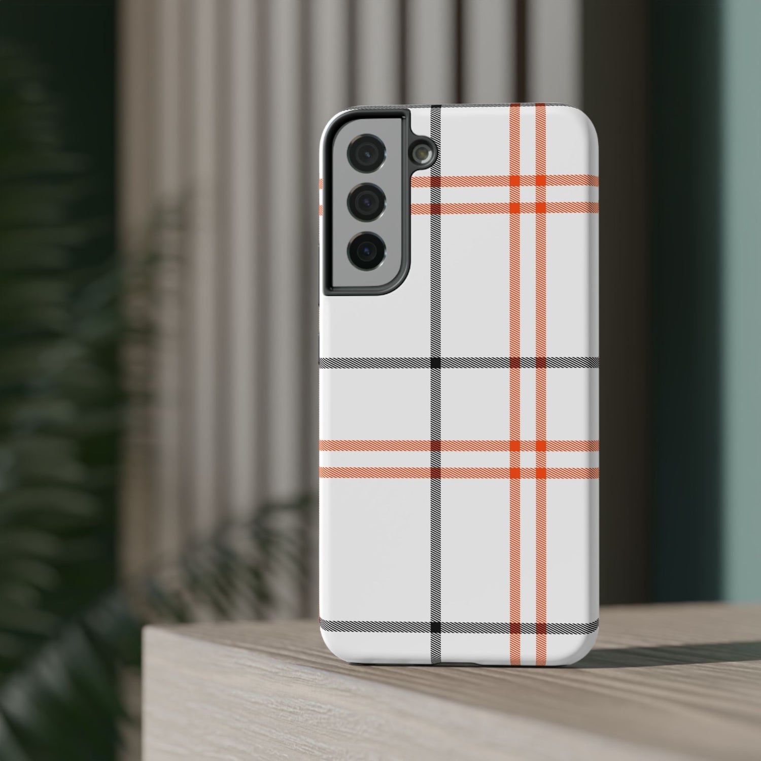 A phone case with a fall tartan plaid pattern in white and orange stripes, featuring a camera module in the center.