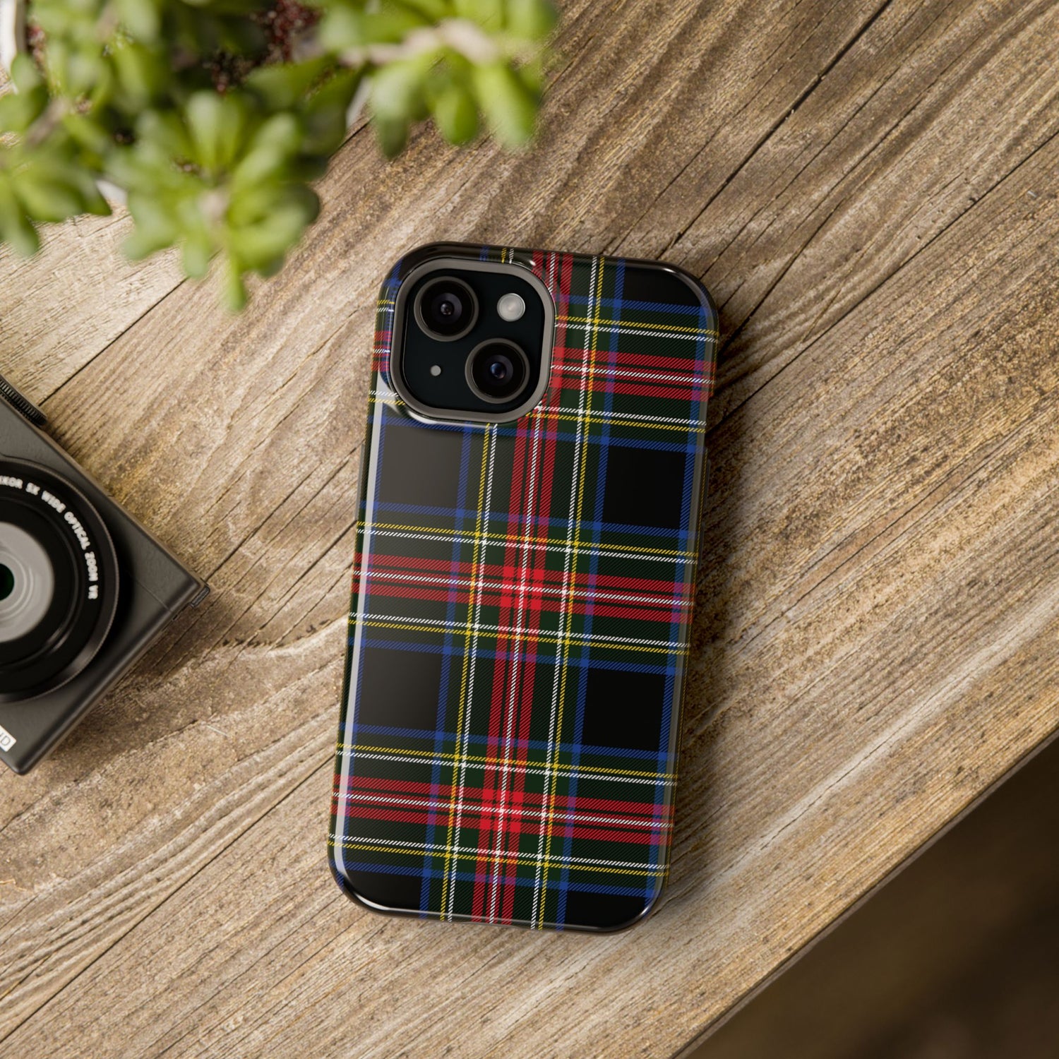 A phone case with a Christmas tartan plaid black pattern, placed on a wooden surface next to a camera, showcasing its design and impact-resistant features.